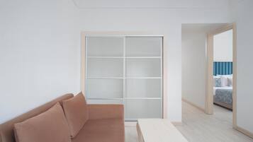 Ein Zimmer mit einem braunen Sofa, einem weißen Tisch und einer großen Schiebetür zu einem weiteren Raum mit einem Bett.