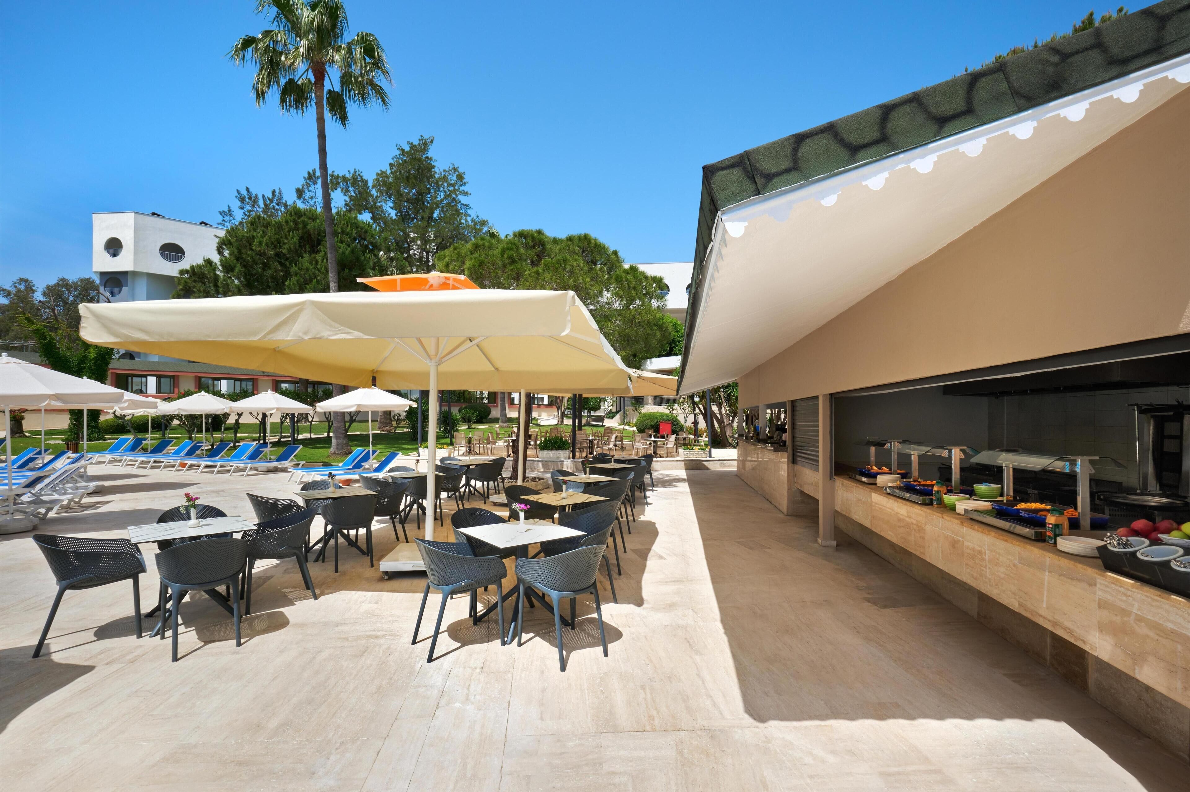 Un espacio al aire libre para comer con mesas, sillas, sombrillas y una barra de buffet.