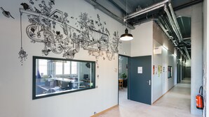 Un espacio de oficina moderno con un gran ventanal, un mural detallado y un pasillo con extintor.