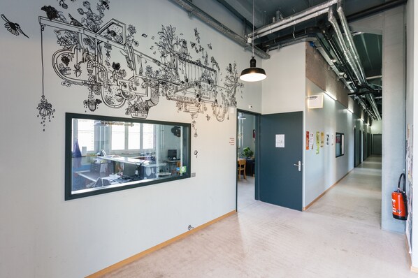 Un espacio de oficina moderno con un gran ventanal, un mural detallado y un pasillo con extintor.