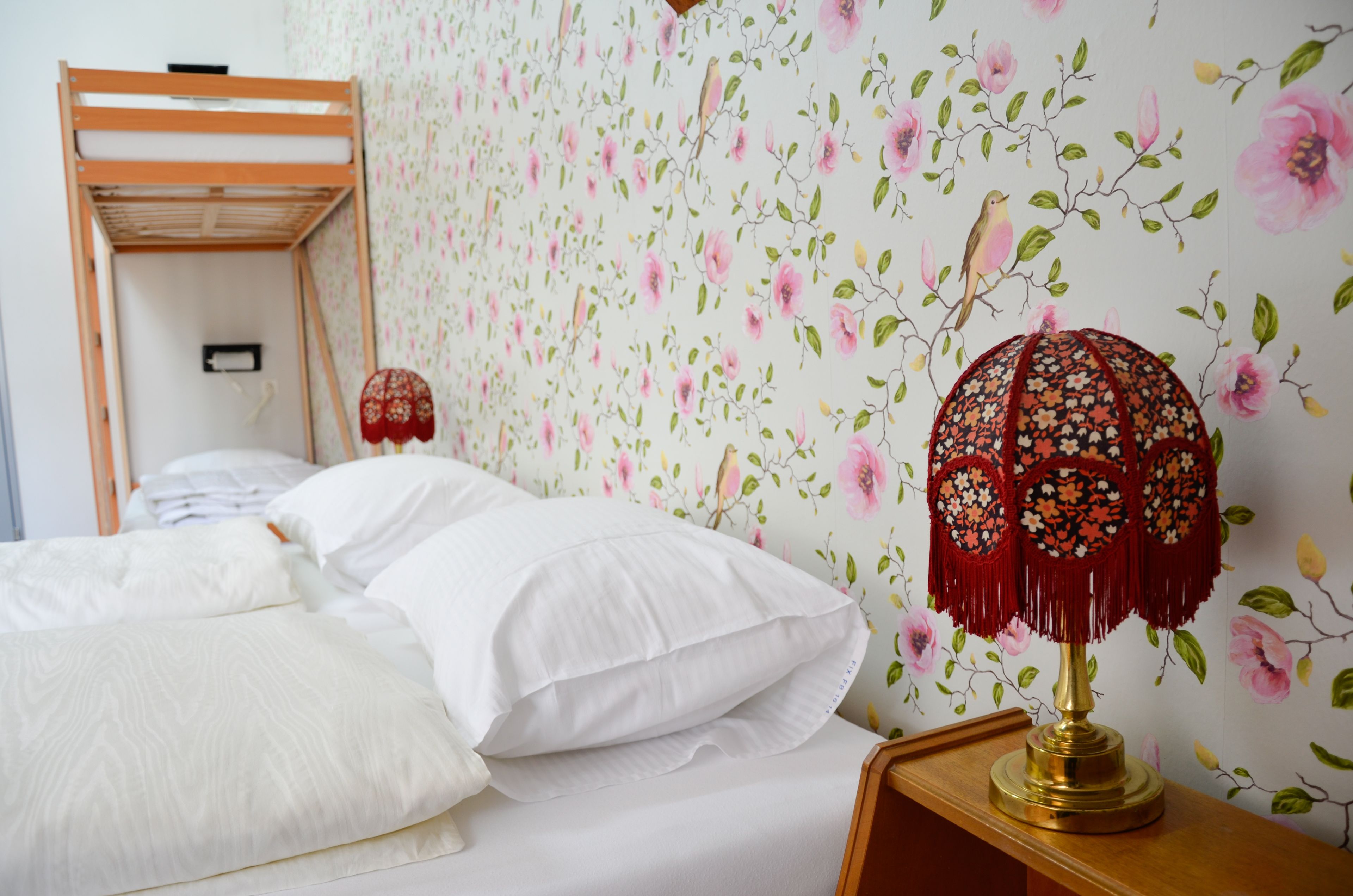 A bedroom with a bunk bed, floral wallpaper, a bedside lamp, and a wooden nightstand.