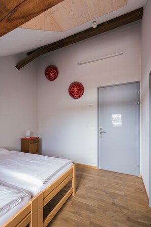 A bedroom with a wooden bed, a small wooden cabinet, a door, and two red spherical decorations on the wall.