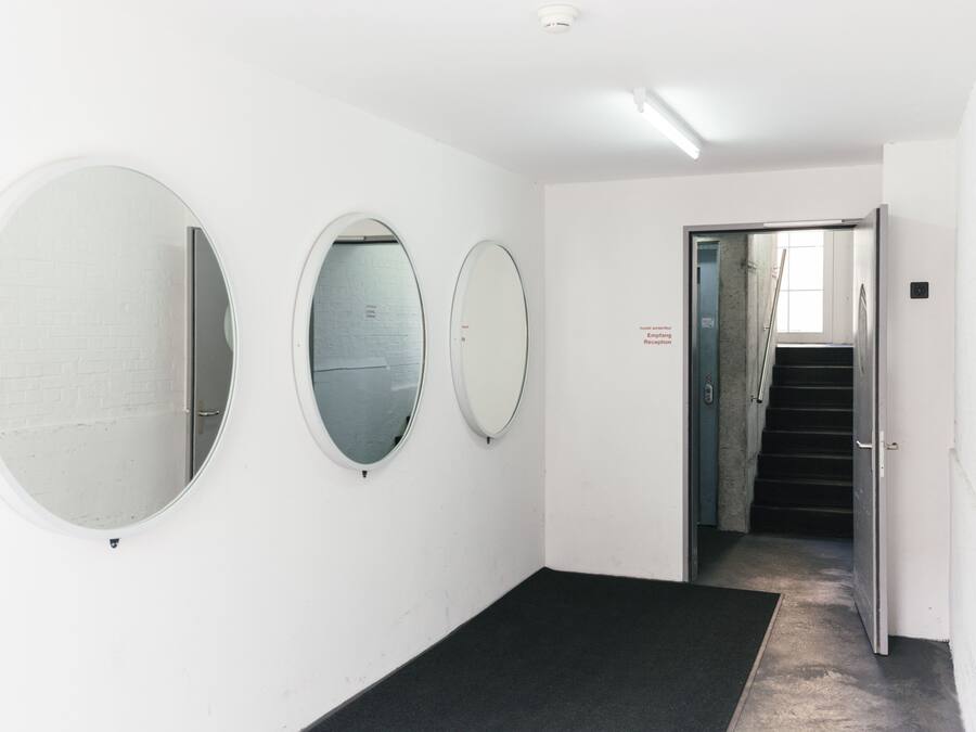 A hallway with three round mirrors on the wall, a black carpet, and a staircase leading to another area.