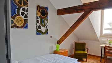 Un dormitorio con una cama individual, un sillón verde, una mesa de madera y dos cuadros abstractos en la pared.