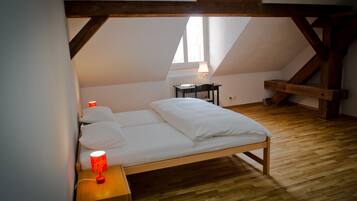 A bedroom with a wooden bed, a nightstand with a red lamp, a chair, and a window with a lamp.