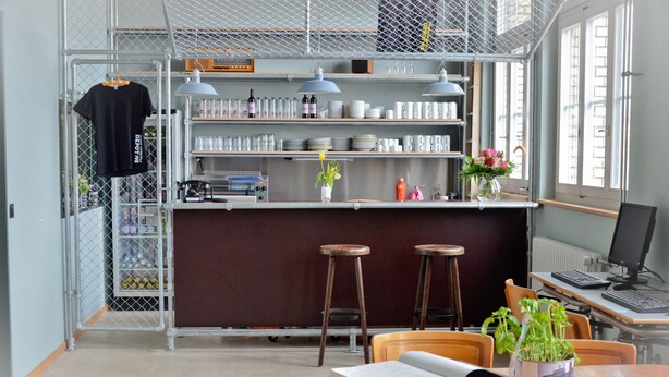 Una cocina moderna con encimera de madera, taburetes de bar y una mesa de comedor. Hay un ordenador sobre un escritorio y una ventana con vistas a la ciudad.