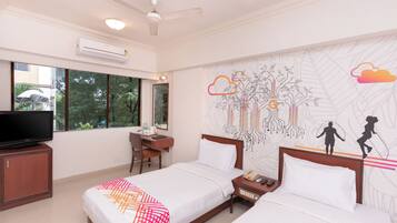 A hotel room with two beds, a desk, a television, and a large window.
