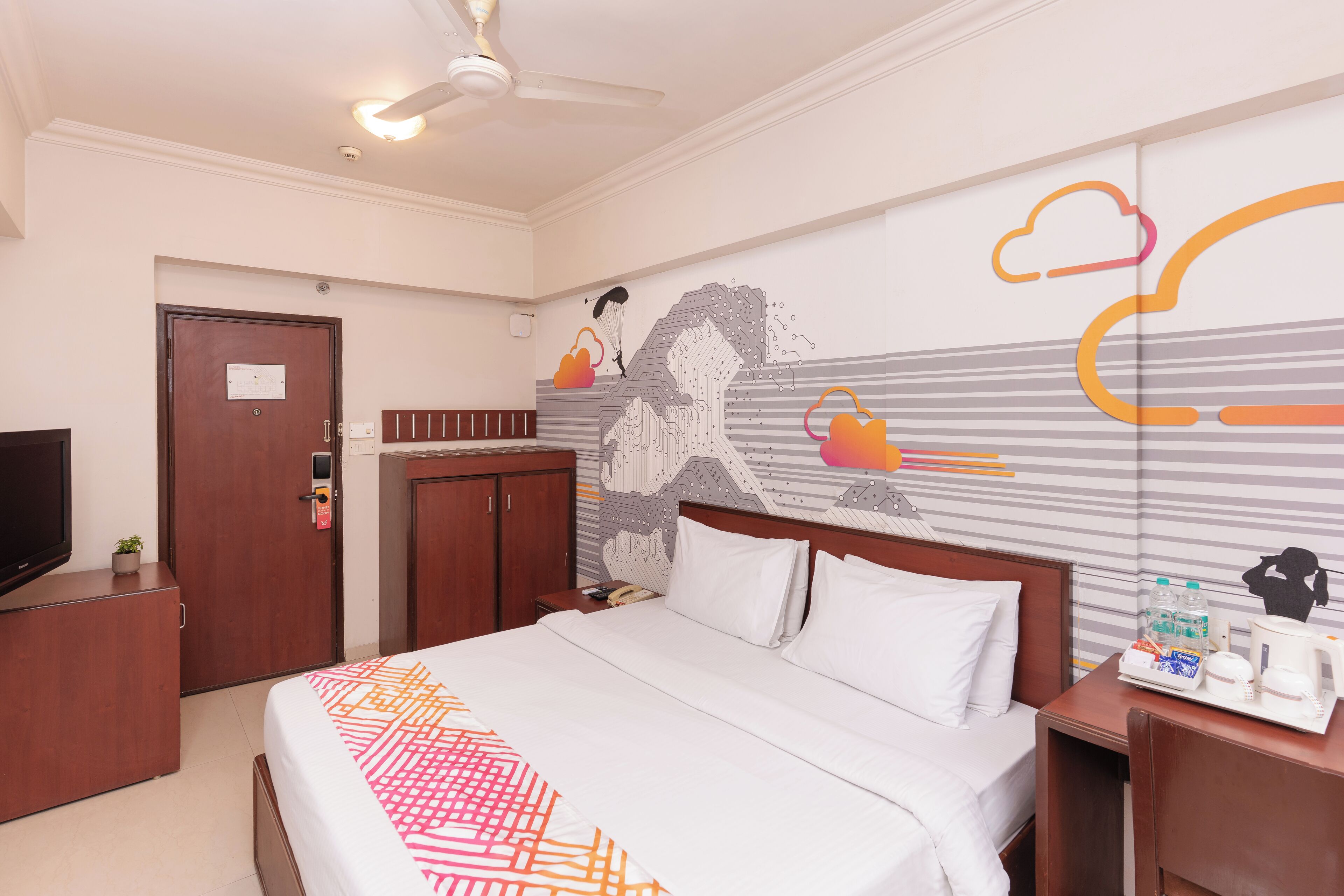 Une chambre d’hôtel équipée d’un lit, d’un bureau avec un téléphone, d’une machine à café et d’un mur orné d’un motif graphique.