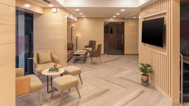 A modern lounge area with a sofa, armchairs, a coffee table, and a TV mounted on a wooden panel wall. - Ginger Hotel Thane (Thane)