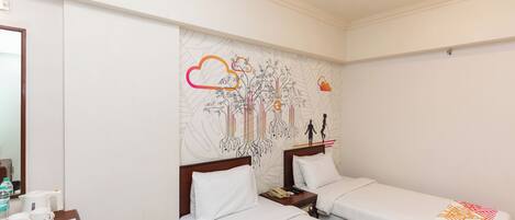 Una habitación de hotel con dos camas individuales, una mesita de noche de madera con un teléfono, una pequeña mesa con cafetera y una pared decorada con un mural.