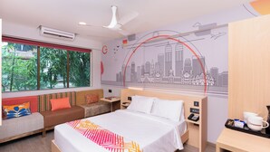 A hotel room with a bed, a sofa, a desk, and a cityscape mural on the wall. - Ginger Hotel Thane (Thane)