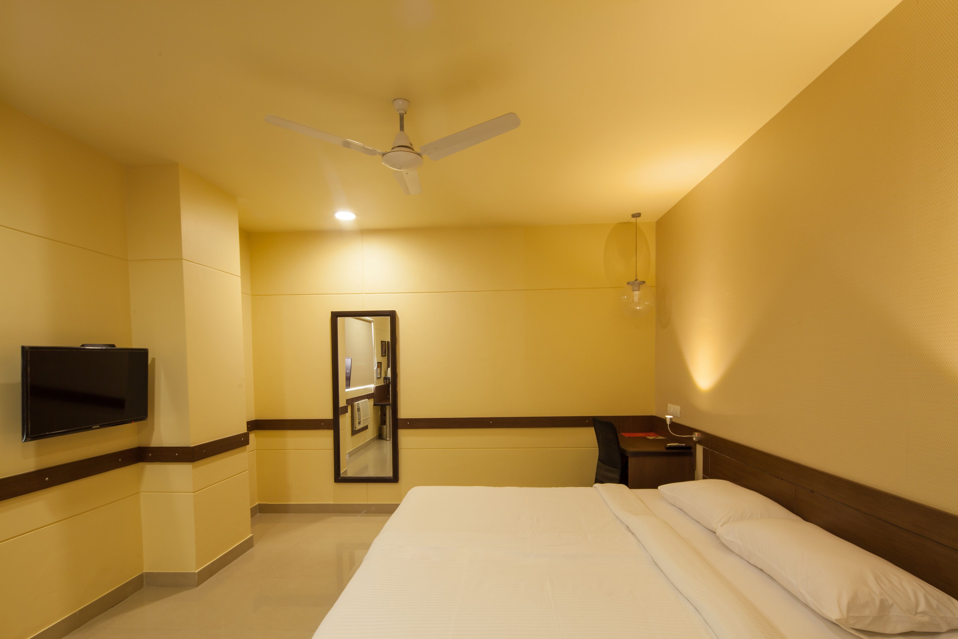 Una habitación de hotel con cama, televisor en la pared, ventilador de techo y espejo.