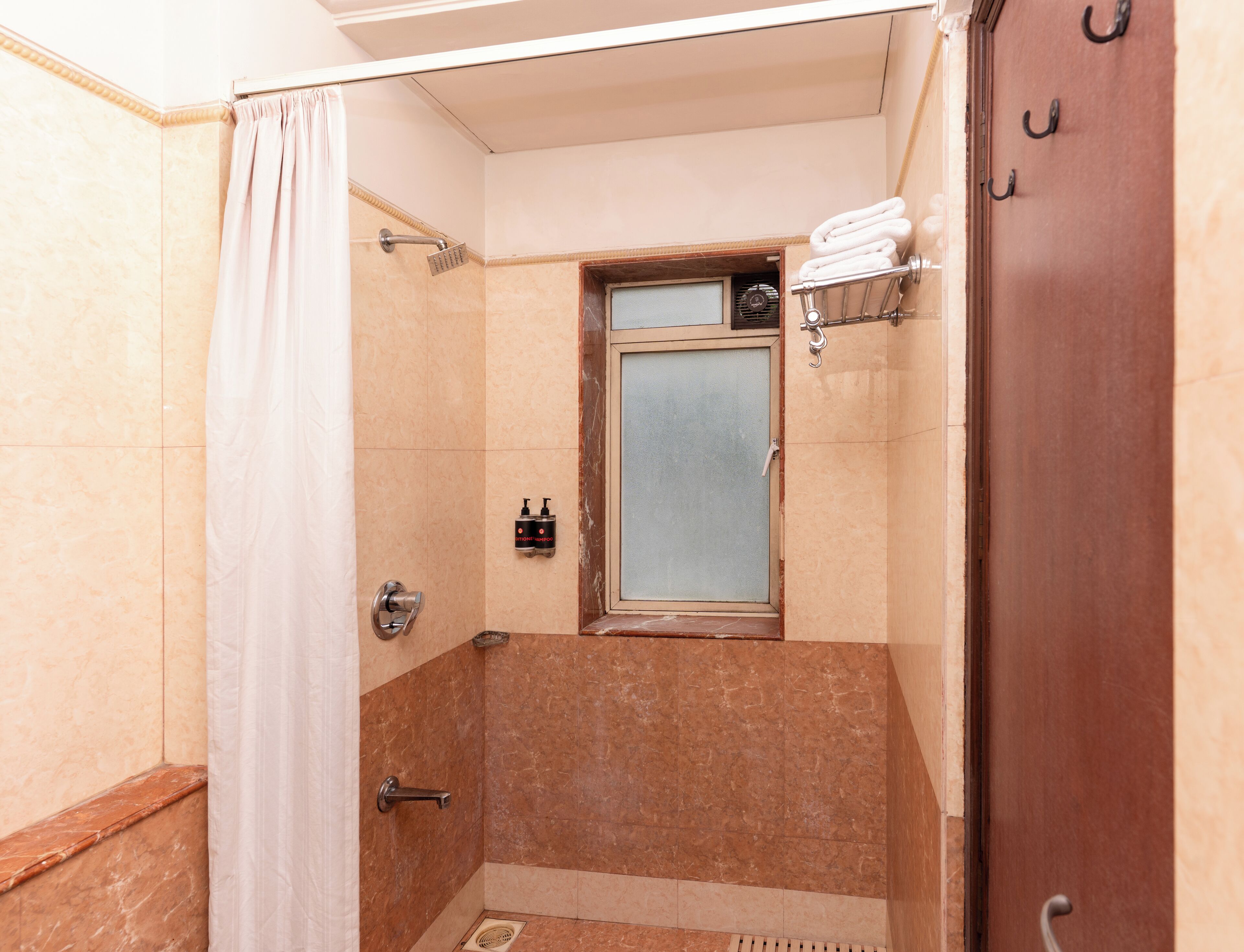 A small bathroom with a shower, a towel rack, and a window.