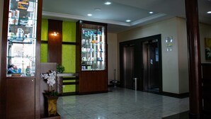 A hotel lobby with a reception desk, a glass display case, an elevator, and a trash bin. - Hotel Exclusivo (Sao Jose dos Pinhais)