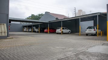 A parking area with covered car bays, a building with a flat roof, and a paved ground.