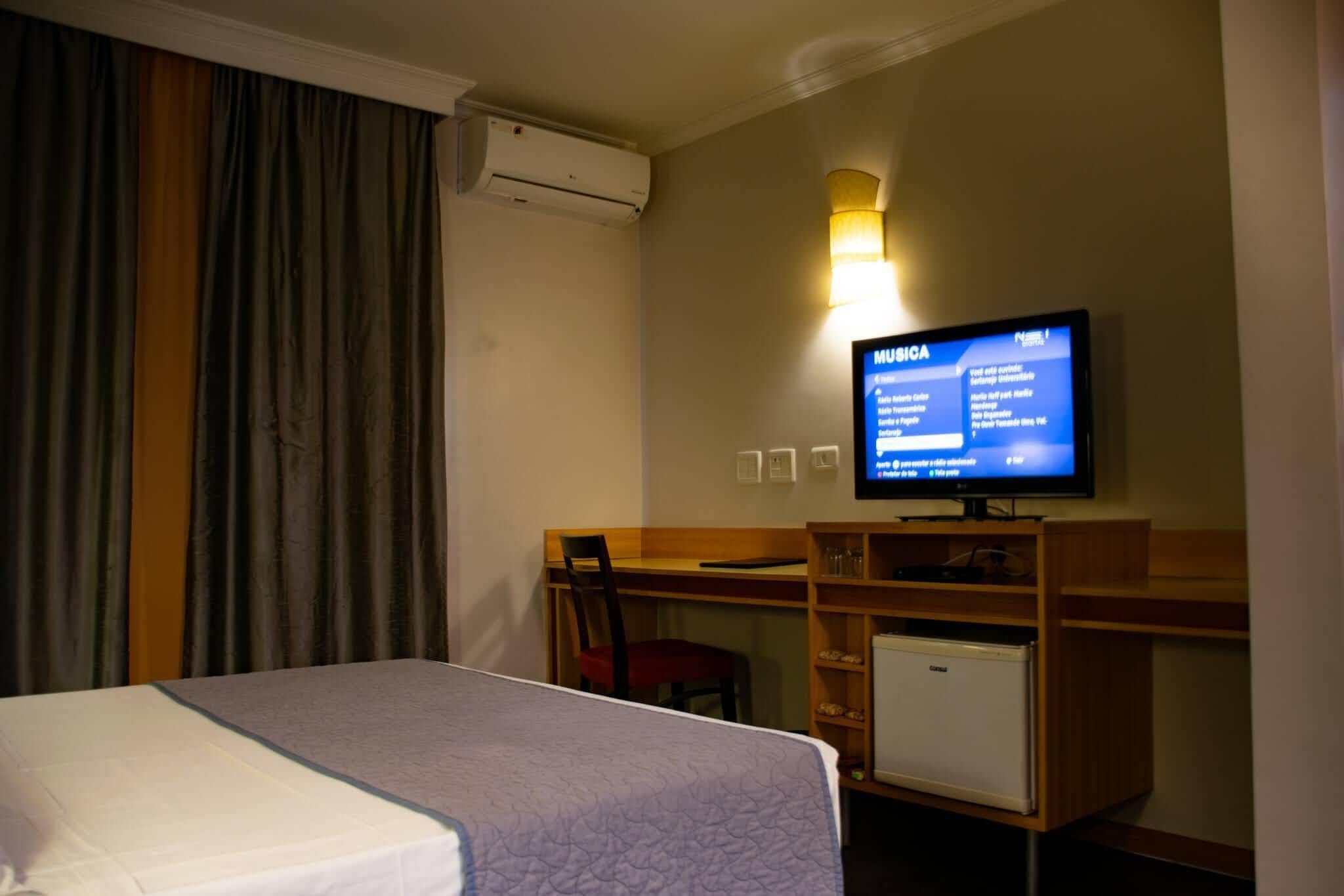 A hotel room with a bed, a desk with a chair, a television, and a minibar.