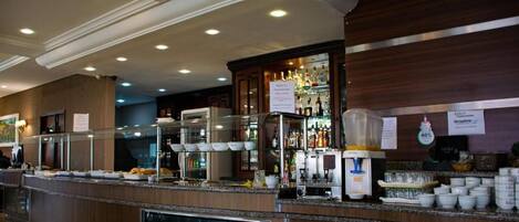 Un área de bufé con diversas opciones de comida, una estación de café y un dispensador de bebidas.