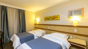 A hotel room with two beds, a desk with a telephone, and a wall-mounted air conditioning unit. - Hotel Exclusivo (Sao Jose dos Pinhais)