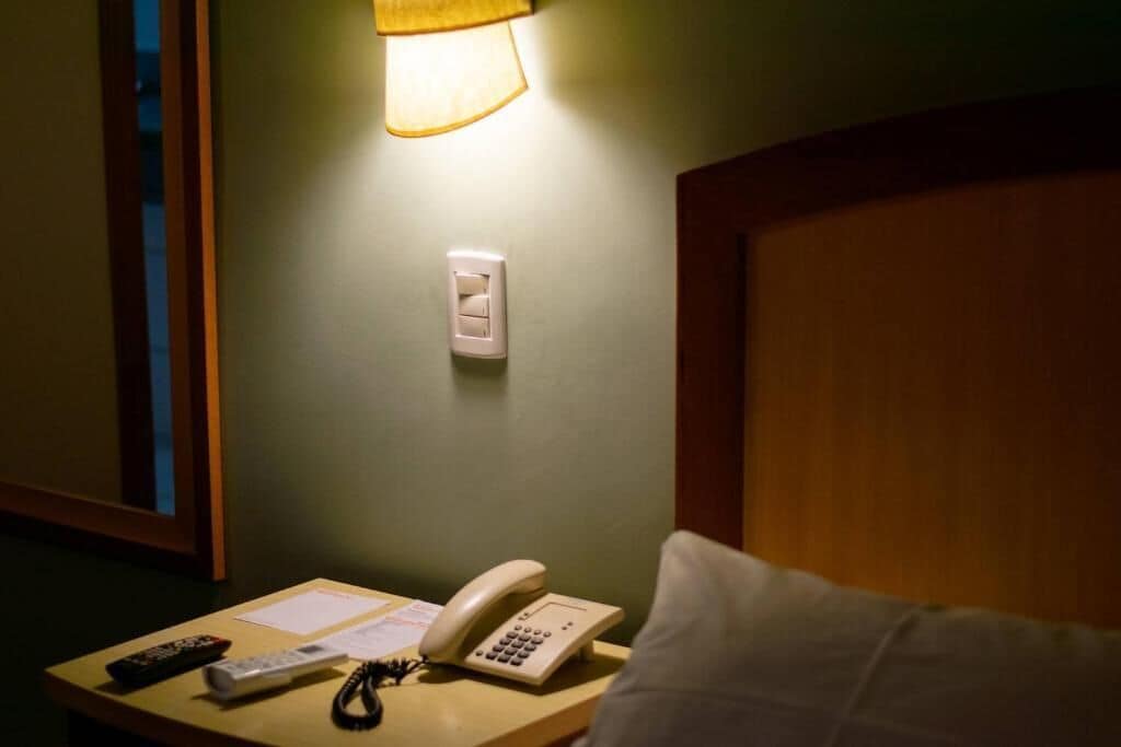 Une chambre d’hôtel équipée d’une table de chevet, d’un téléphone, d’une télécommande et d’une lampe.