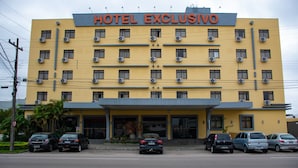 A multi-story hotel building with a yellow facade, multiple air conditioning units, and a sign reading "HOTEL EXCLUSIVO". - Hotel Exclusivo (Sao Jose dos Pinhais)