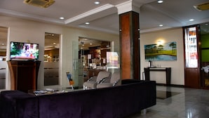 A lobby with a reception desk, a television, a seating area, and a painting on the wall. - Hotel Exclusivo (Sao Jose dos Pinhais)