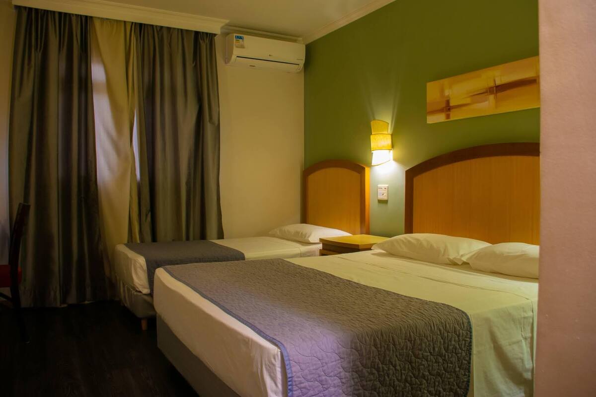 A hotel room with two beds, a wooden headboard, a wall-mounted air conditioner, and a lamp.
