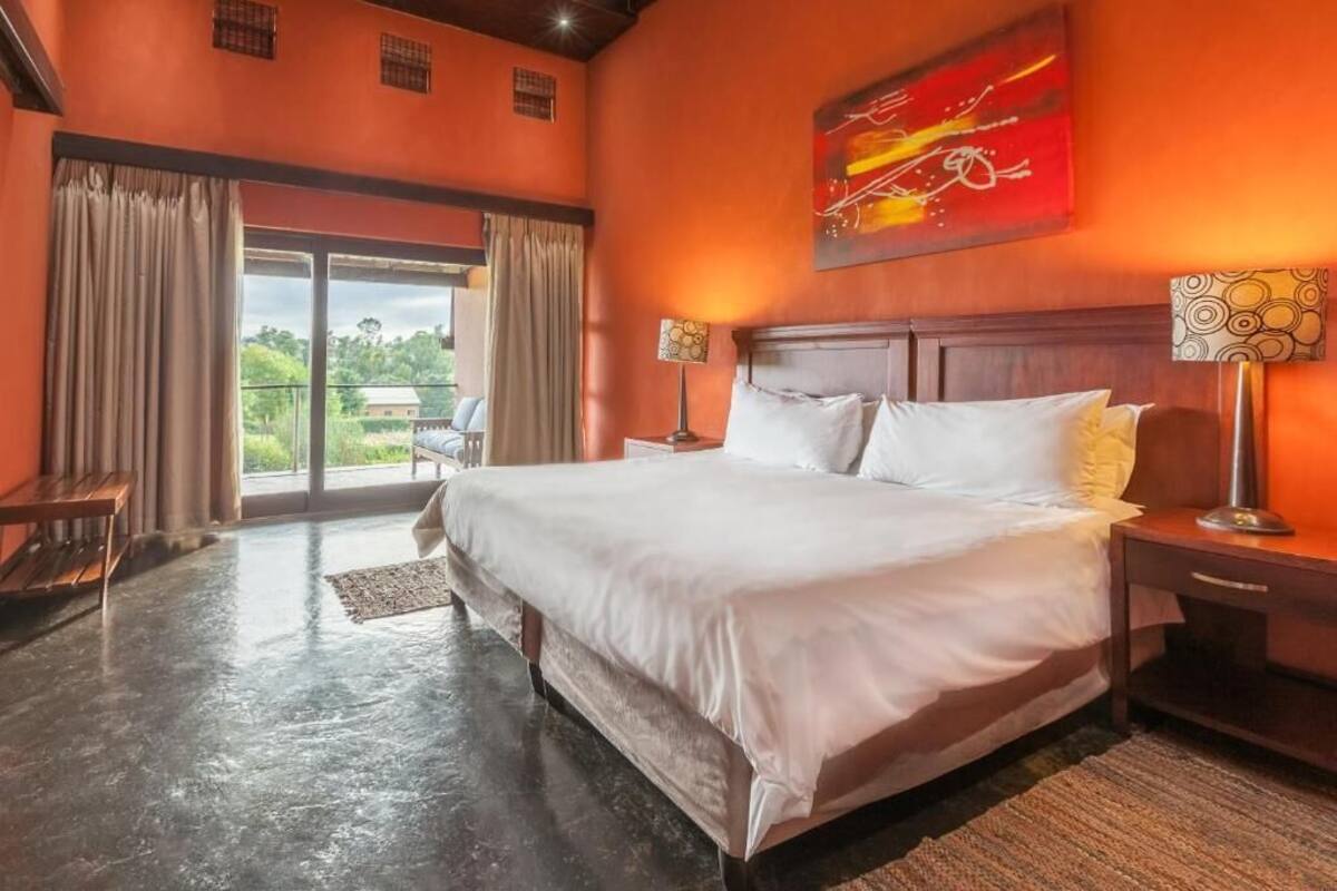 A large bed with white linens in a room with orange walls, a wooden headboard, and a view through a glass door to the outdoors.
