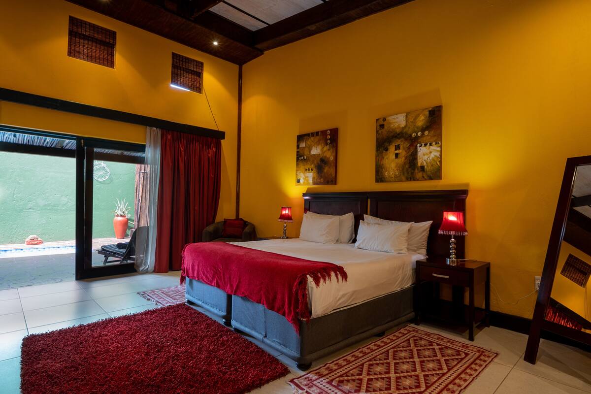 A bedroom with a large bed, two bedside tables with lamps, a red carpet, and a view through a sliding door to an outdoor area.