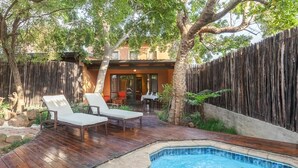 Un patio trasero con terraza de madera, un jacuzzi y dos sillones de descanso.