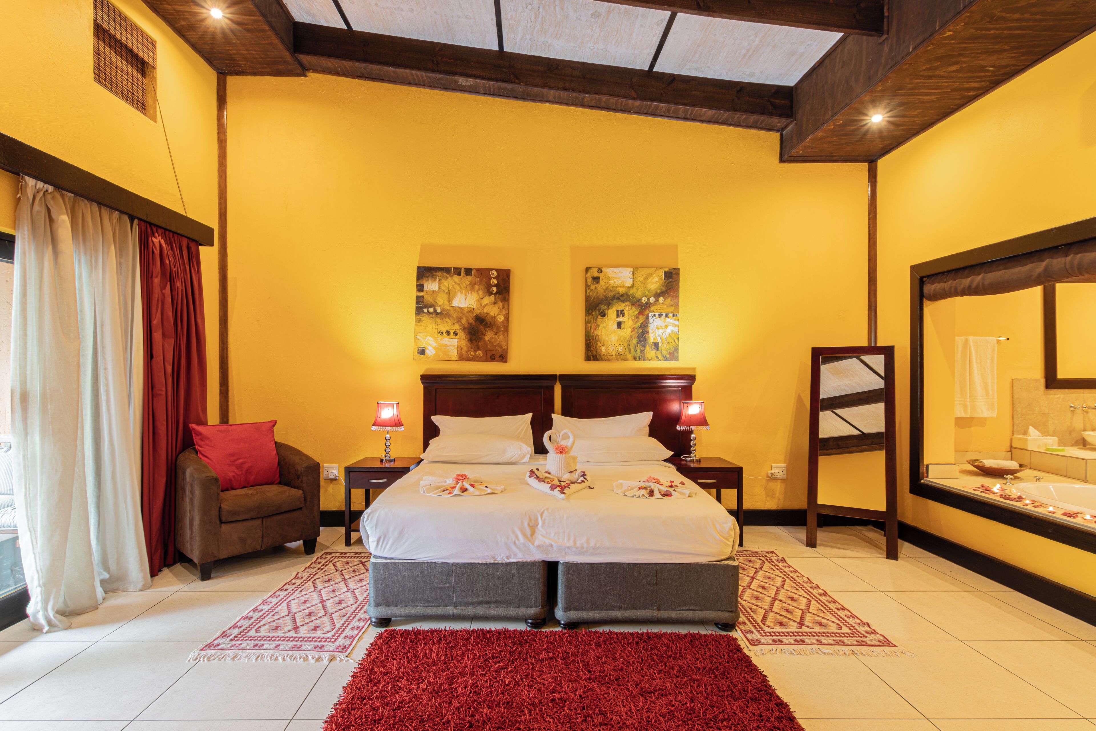 Une chambre d’hôtel avec un grand lit, deux tables de chevet, un tapis rouge et des œuvres d’art accrochées aux murs.