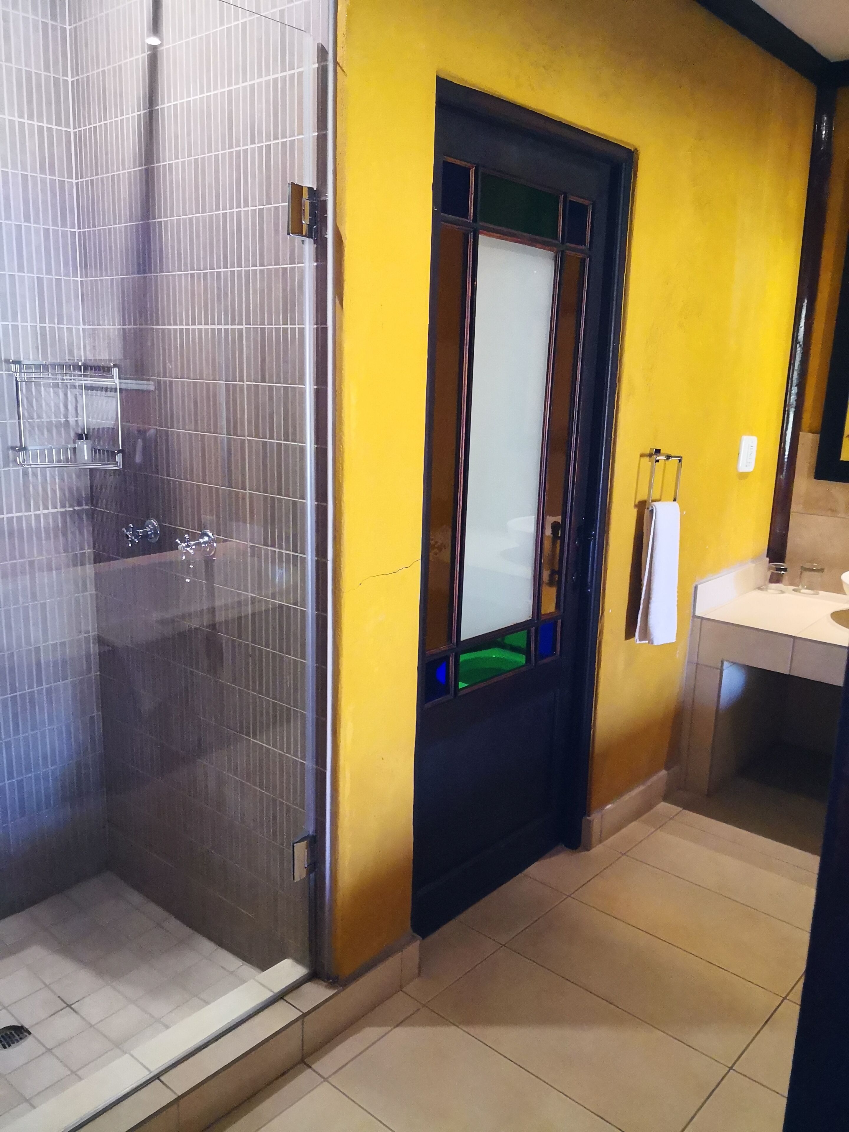A bathroom with a glass shower enclosure, a yellow wall, a black door, and a white sink.