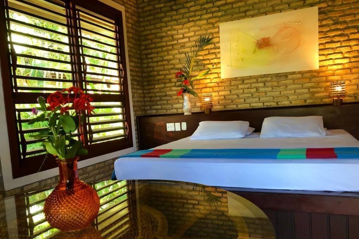 Een hotelkamer met een bed, een glazen tafel, een bloemenvaas en een bakstenen muur.