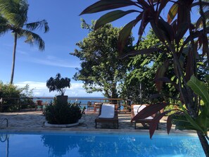 Zona junto a la piscina con sillas de descanso y vista al océano.