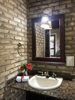 Un baño con encimera de granito, un lavabo blanco, un espejo con marco oscuro y una lámpara colgante.