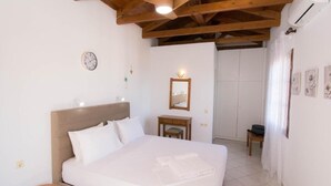 A bedroom with a large bed, a bedside table, a small chair, a mirror, and a door leading to another room. - Rena Apartments Gouves (Hersonissos)
