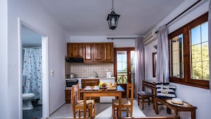 A compact room with a kitchenette, a dining table with chairs, a bed with patterned bedding, and a window with curtains. - Rena Apartments Gouves (Hersonissos)