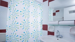 A bathroom with a white sink, a glass shelf, a mirror, and a shower curtain with a polka dot pattern. - Rena Apartments Gouves (Hersonissos)
