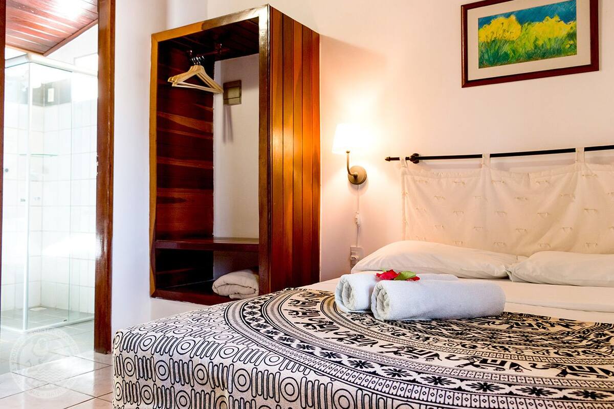 A hotel room with a bed, a wooden wardrobe, a shower, and a painting on the wall.