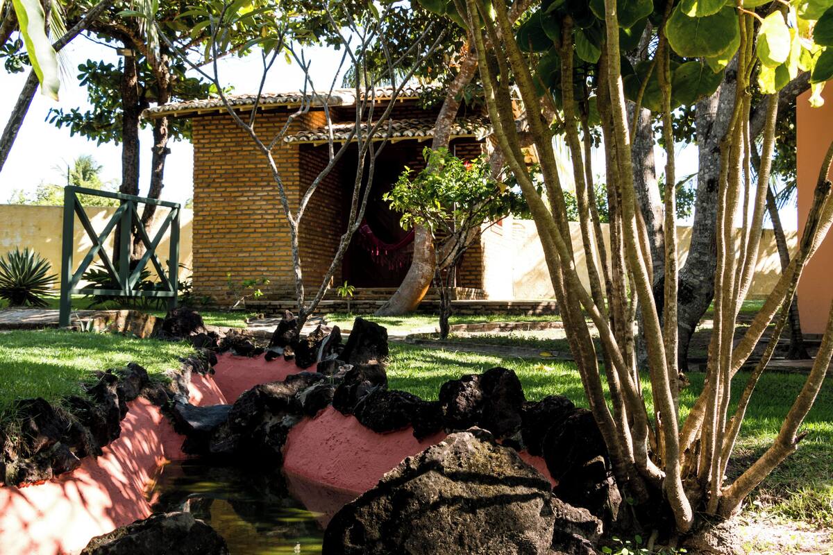 A garden with a small pond, a brick building, and a tree.
