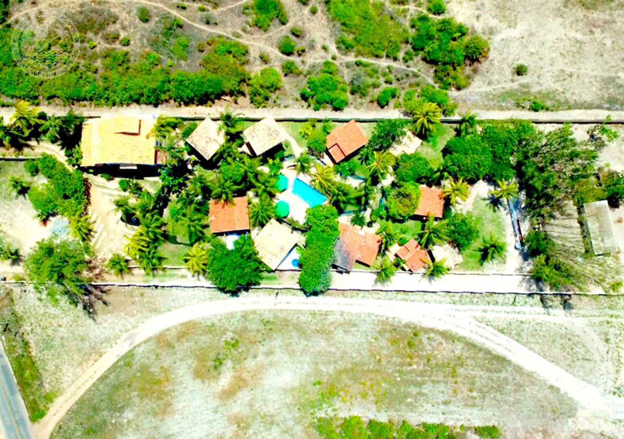 An aerial view of a resort with multiple buildings, a central pool, and surrounding greenery.