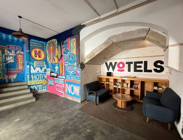 Un hall d’hôtel moderne agrémenté d’une fresque colorée, d’un comptoir d’accueil, d’un espace salon et d’un escalier.