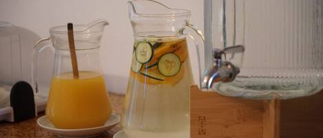 A pitcher with a straw and sliced cucumbers, a glass pitcher with a straw, and a water dispenser on a wooden surface.