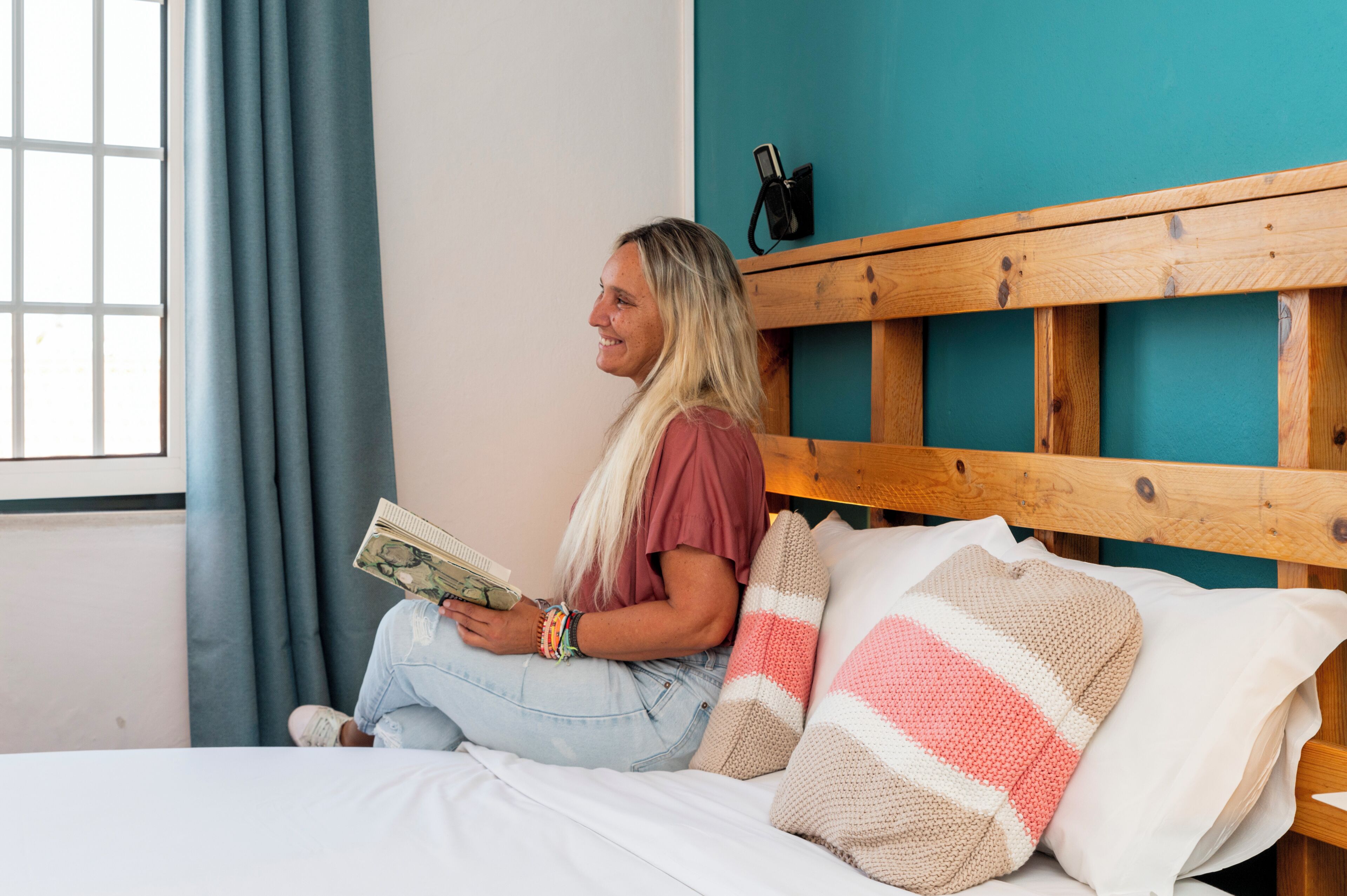 Una persona sentada en una cama con cabecera de madera, sosteniendo un libro.