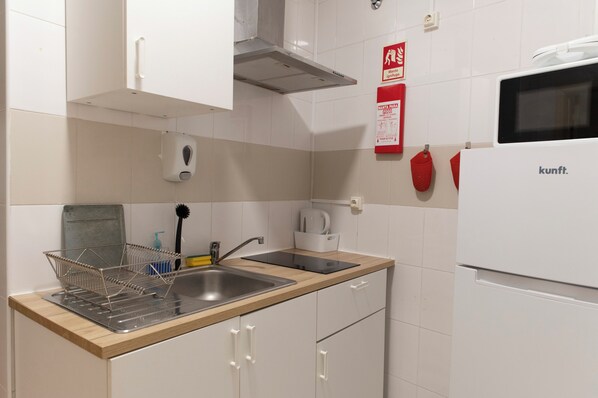 Una cocina con un lavamanos de acero inoxidable, un microondas y un extintor rojo.