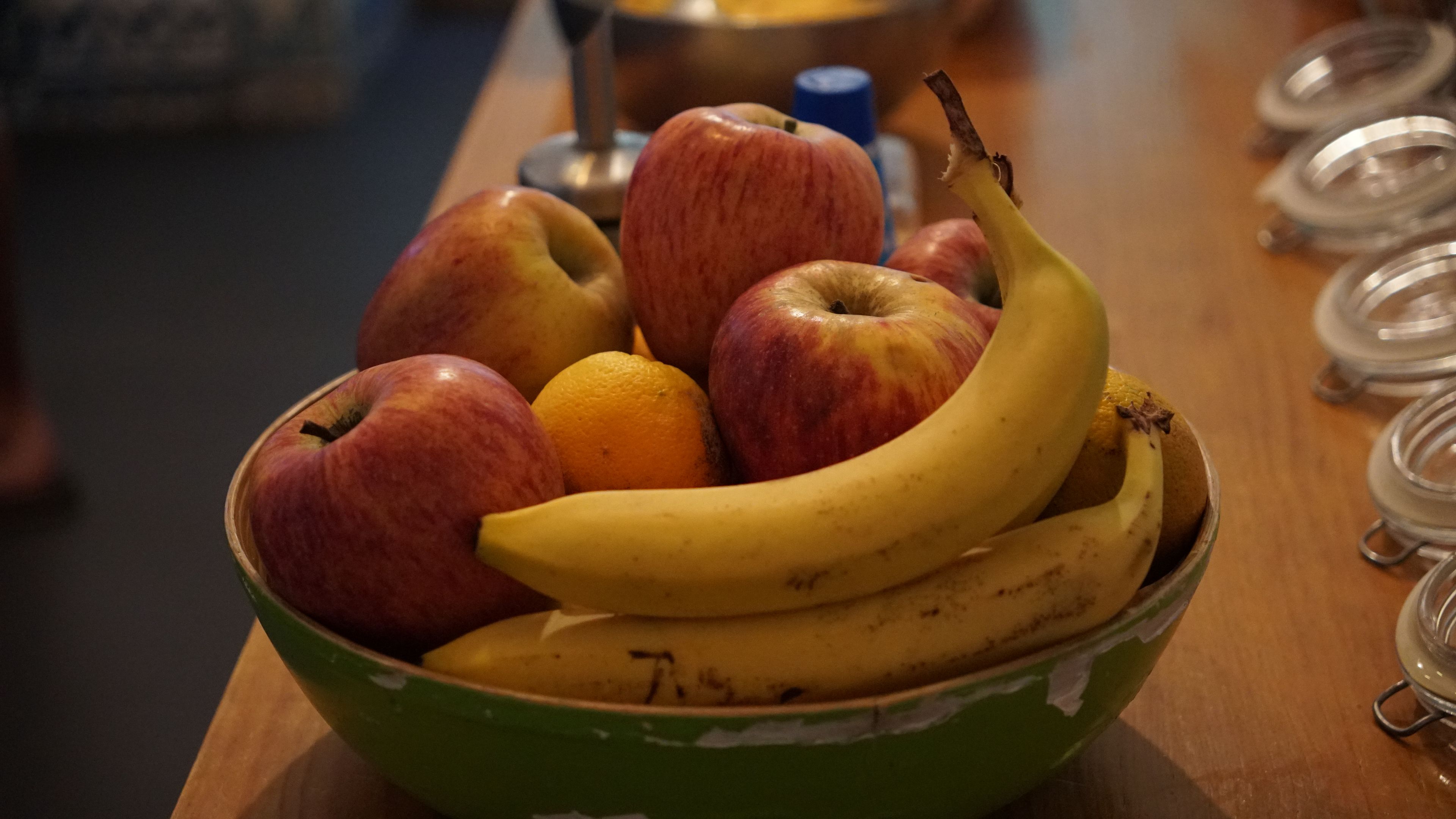 Un bol con manzanas, una naranja y un plátano sobre una mesa de madera.