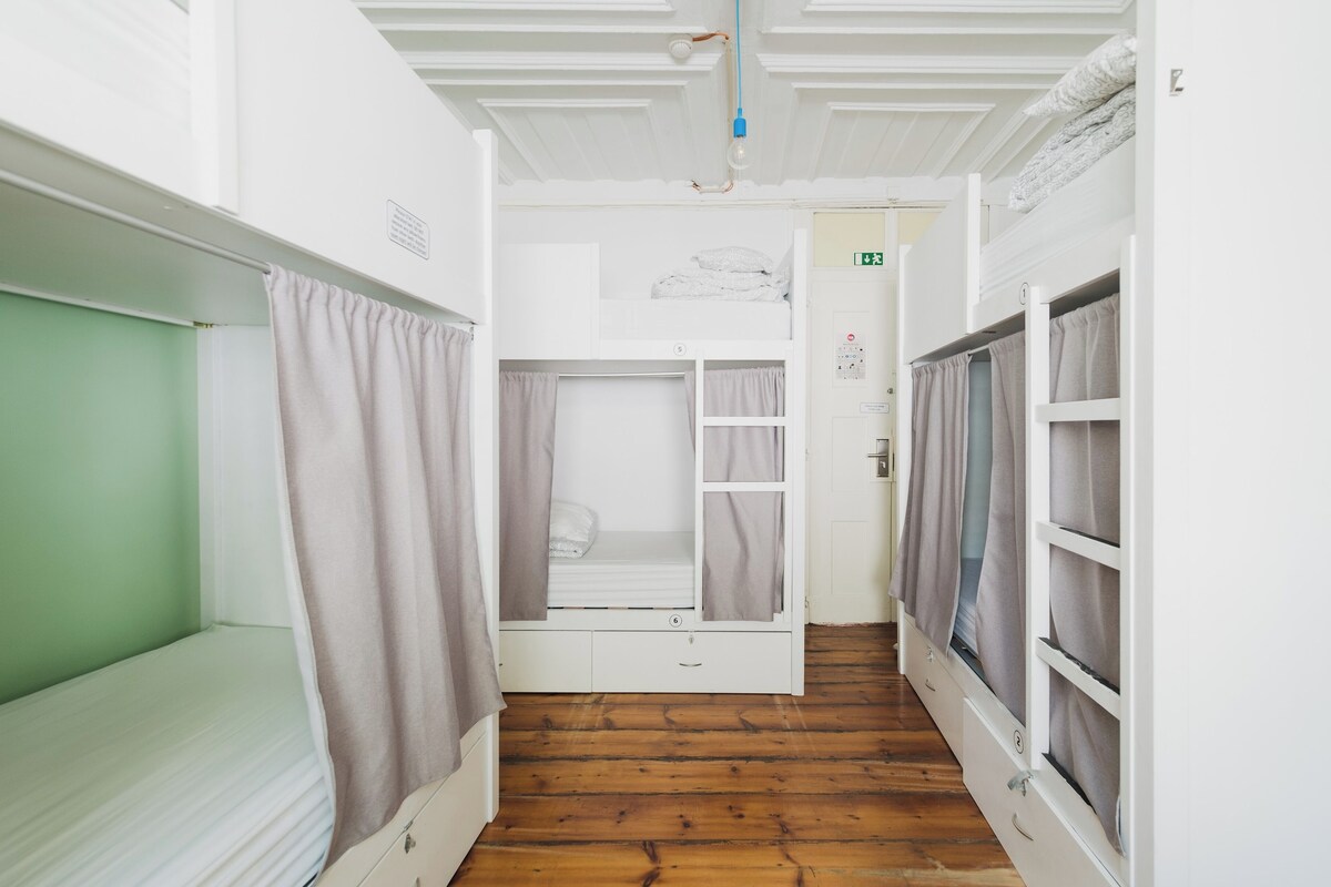 A narrow corridor with bunk beds on either side, wooden flooring, and a white ceiling with ventilation.
