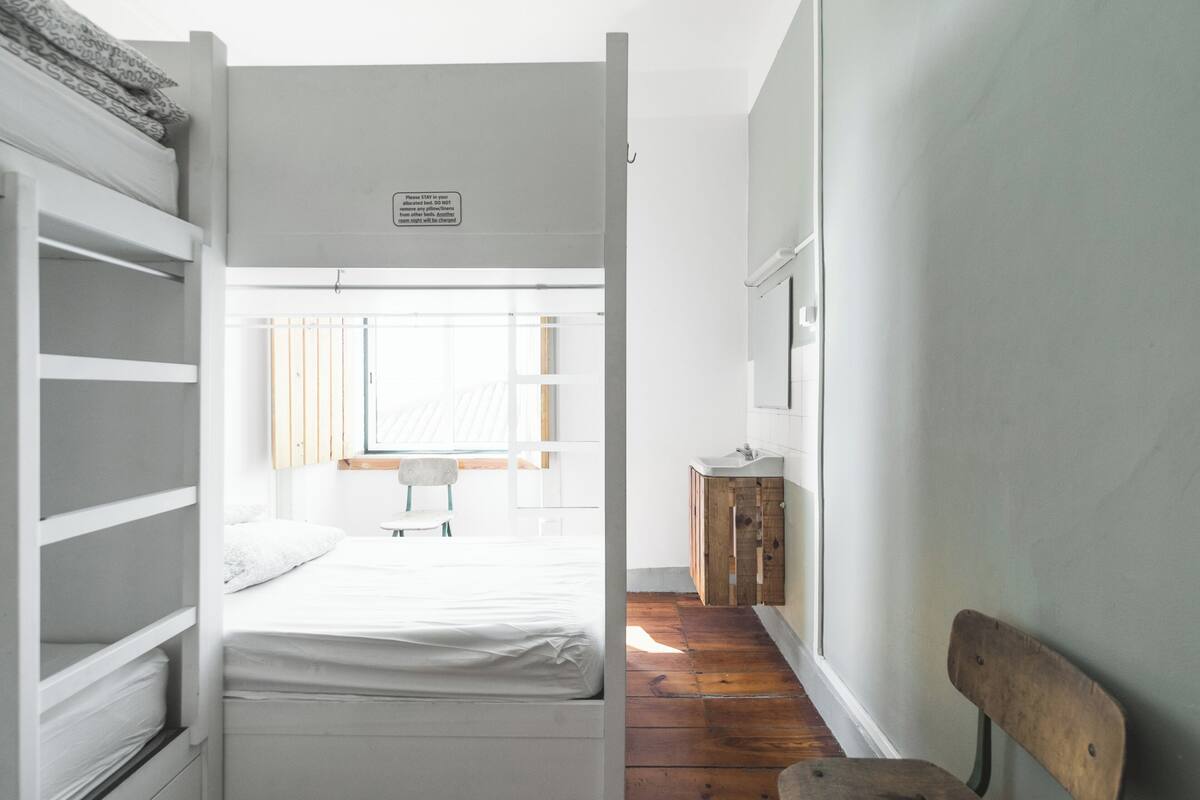 Un dormitorio con literas, suelo de madera, un escritorio pequeño y una silla.