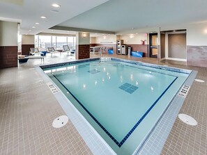 Una amplia piscina interior con agua cristalina, rodeada de sillones de descanso y una terraza con sol.