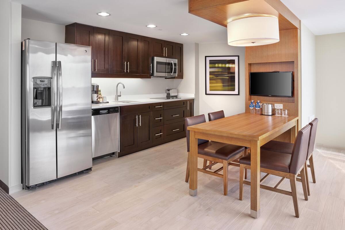 A modern kitchen with stainless steel appliances, wooden cabinets, and a dining area with a wooden table and chairs.