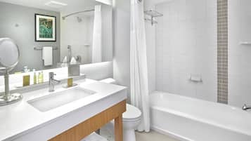 Un baño moderno con un lavamanos, espejo y tocador blancos, un inodoro y una bañera con zona de ducha.